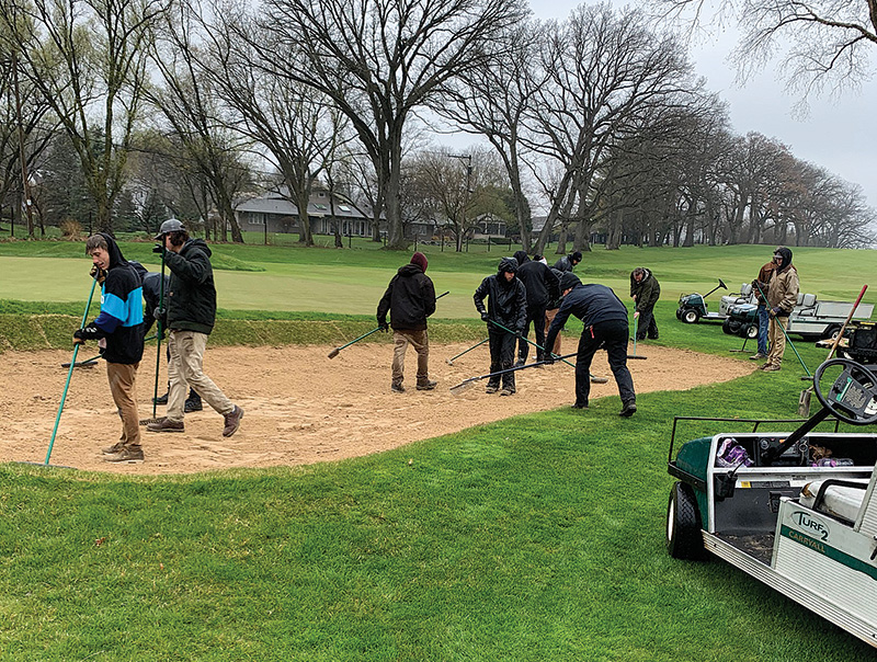 Employees cleaning up at Lake Geneva Country Club. Employees are wearing black and working under an overcast sky.