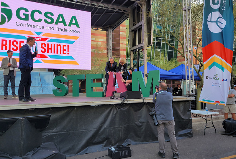 Michael Hoffman and Tamara Hoffman adding an A to a STEAM sign on the main stage of the GCSAA Conference and Trade Show at the Canyon on Third