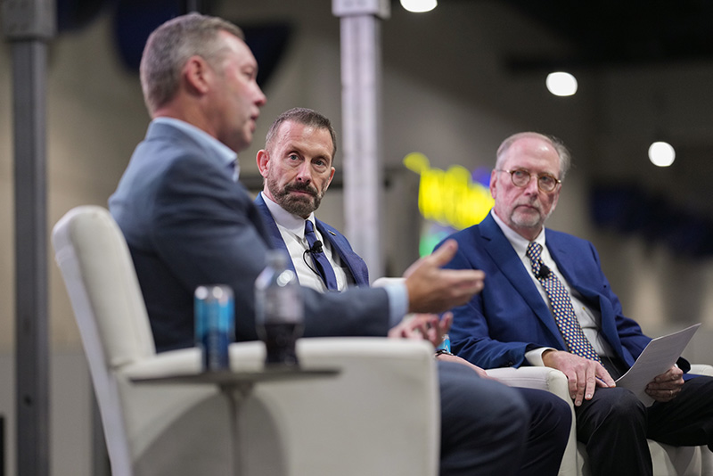 Three men sit together talking on a stage.