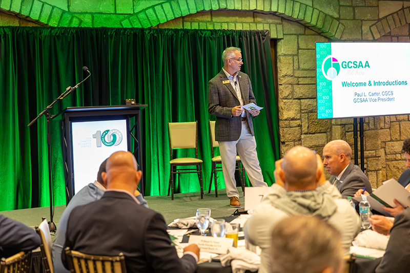 a large group of men sitting inside a hotel conference room in front of a stage with green lighting