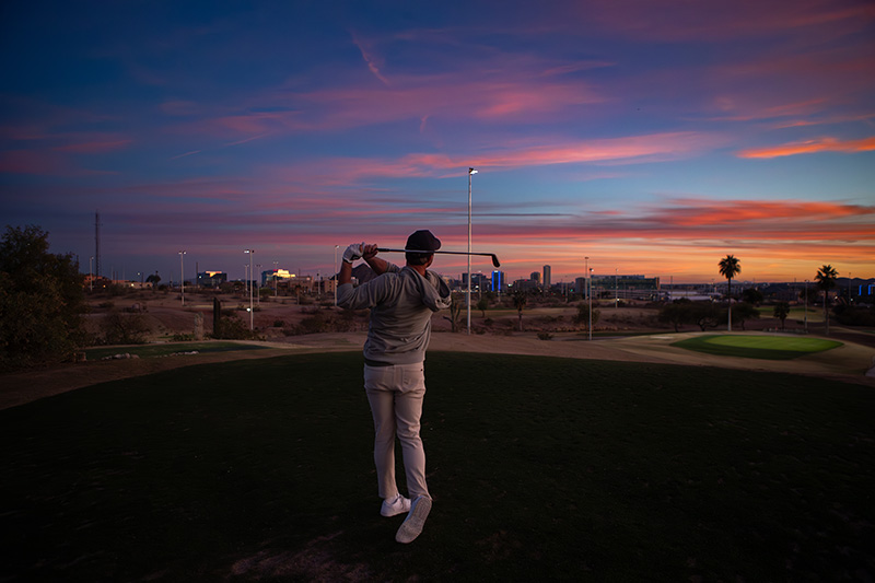 Man teeing off on a golf course at night. The course is lit for play