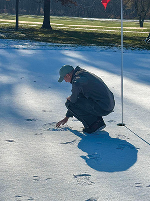 Man examining snow on a golf course