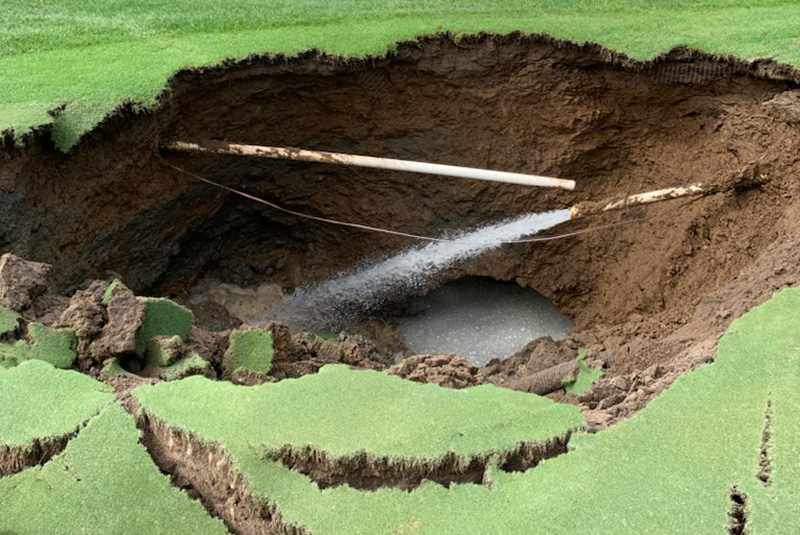 Large sinkhole on a putting green with broken pipe flooding the hole