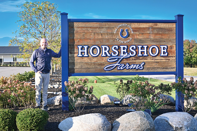 Chase Bonnell stands next to the Horseshoe Farms sign at the entrance to the club