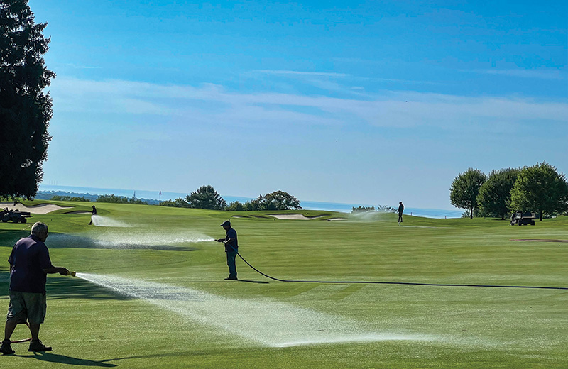Men watering a golf fairway with a hose during the daytime