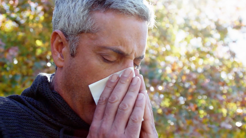Man outside using a tissue to blow his nose