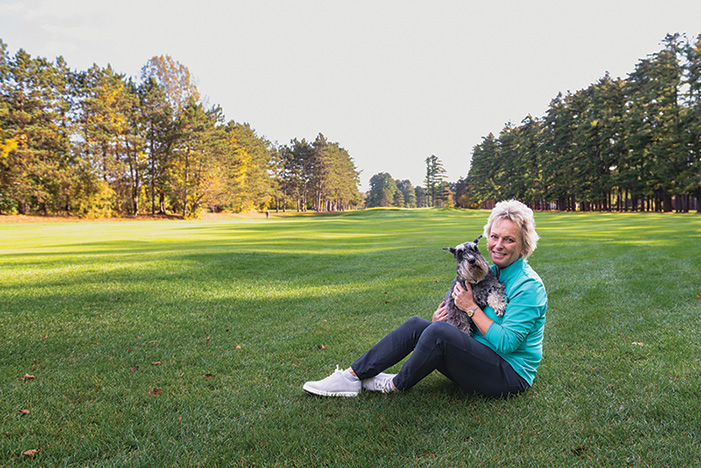 Dottie Pepper sitting on a golf course with a small grey dog