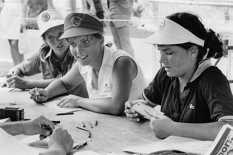 Black and white photograph of three women sitting at a table. Dottie Pepper sits in the middle.