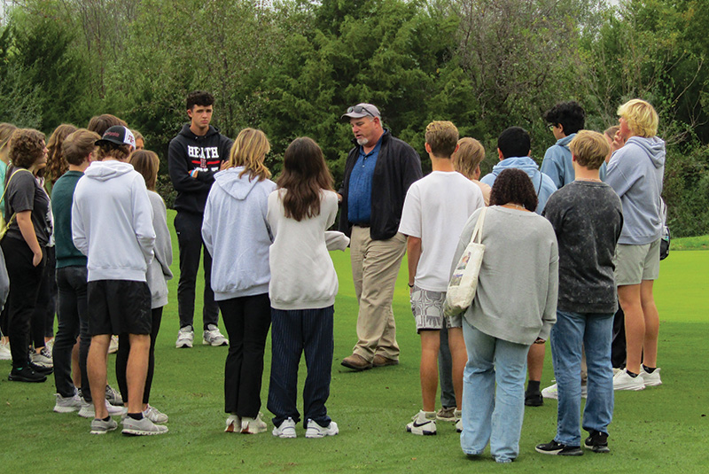 Man teaching a group of children outdoors on a golf course