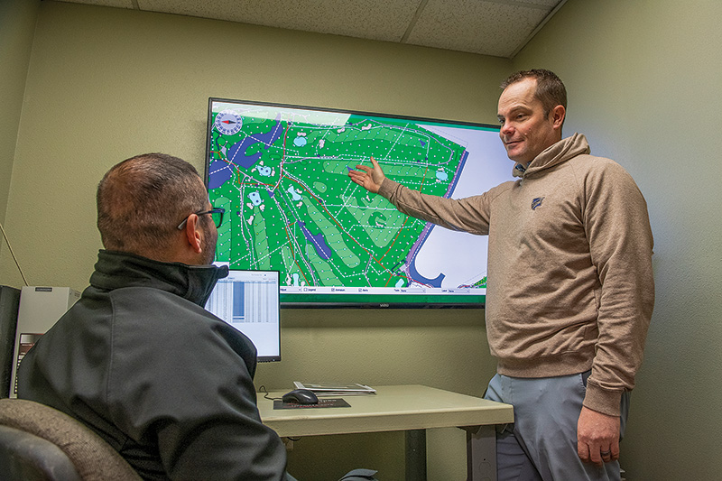 Two men sitting in a maintenance office discussing the data displayed on a digital screen behind them