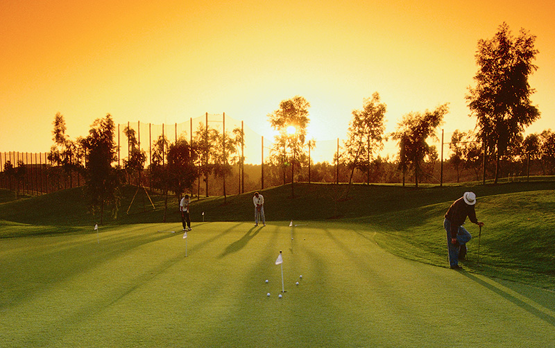 Three players on a putting green at sunset