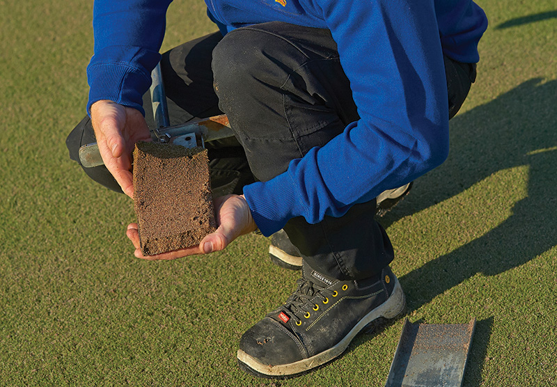 Man depicted from waist down performing a soil test on a golf course